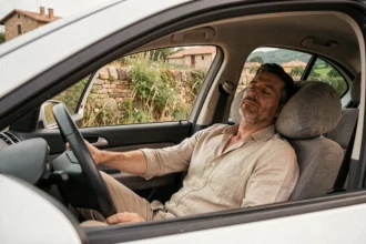 Homme dormant dans sa voiture garée en bord de route en Italie, appuie-tête avec coussin de voyage